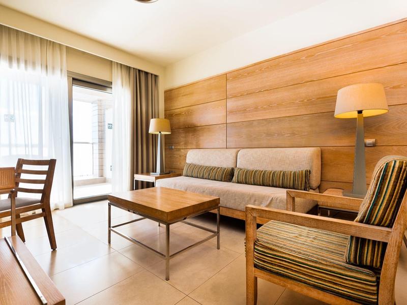 Jasny salon z drewnianymi meblami, sofami i dużym oknem z zasłonami.