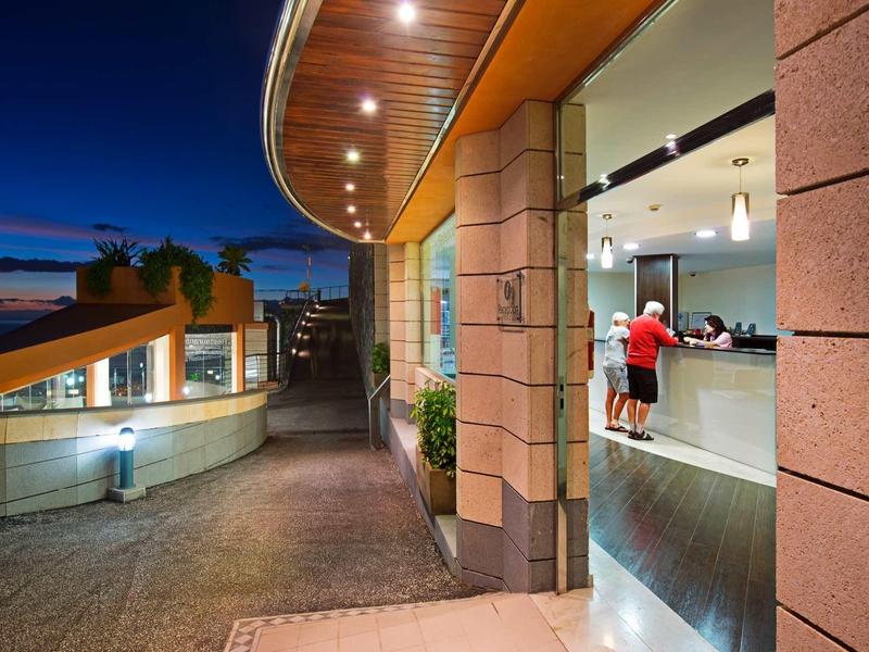 Moderner Eingang mit beleuchtetem Vordach, großem Fenster und Gehweg in warmem Abendlicht.