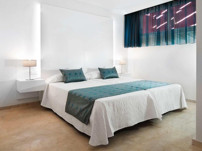 Modernes Schlafzimmer mit großem Bett, weißer Bettwäsche, grünen Details und zwei Nachttischlampen.