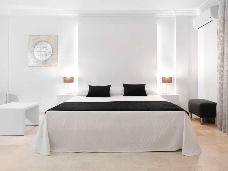 Helles Schlafzimmer mit großem Bett, schwarzer Bettdecke, weißen Wänden und minimalistischer Dekoration.