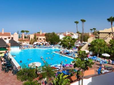 Grande piscina dell'hotel con lettini e ombrelloni, circondata da palme e edifici sotto un cielo limpido.