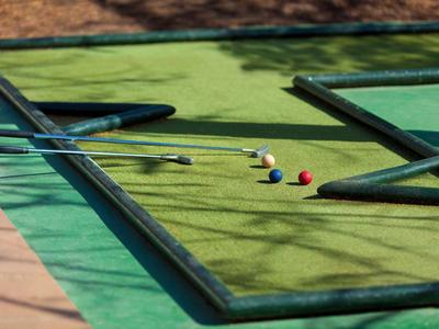 Campo da mini golf all'aperto con palline, mazze e ombre di alberi nel pomeriggio.