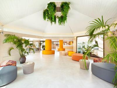 Luminosa hall dell'hotel con piante e aree salotto moderne arancioni e grigie.