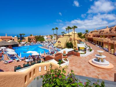 Vista di una vivace piscina dell'hotel con ombrelloni e più edifici sotto un cielo blu.