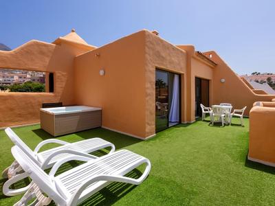 Terrazza con lettini, vasca idromassaggio e zona soggiorno circondata da muri arancioni.