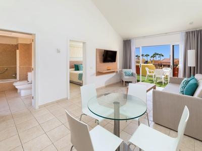 Soggiorno moderno con divano, tavolo in vetro, TV e vista su terrazza e giardino.