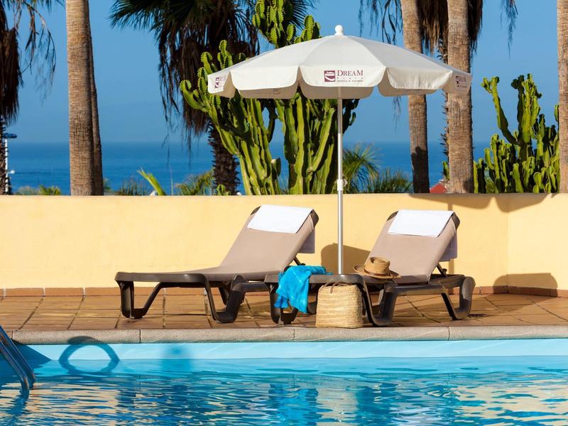 Due sdraio con ombrellone accanto a una piscina con vista su palme e oceano.