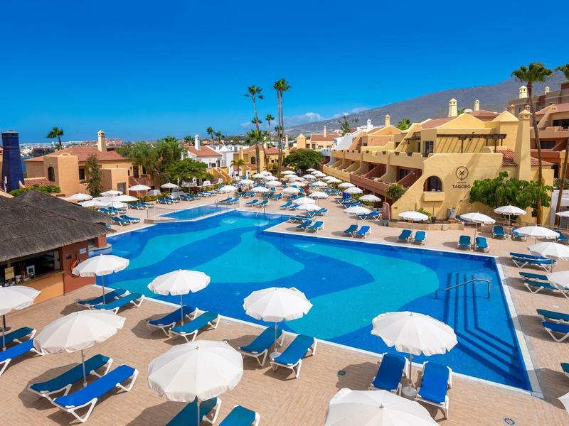 Grande piscina all'aperto con lettini blu e ombrelloni bianchi in hotel sotto cielo sereno.