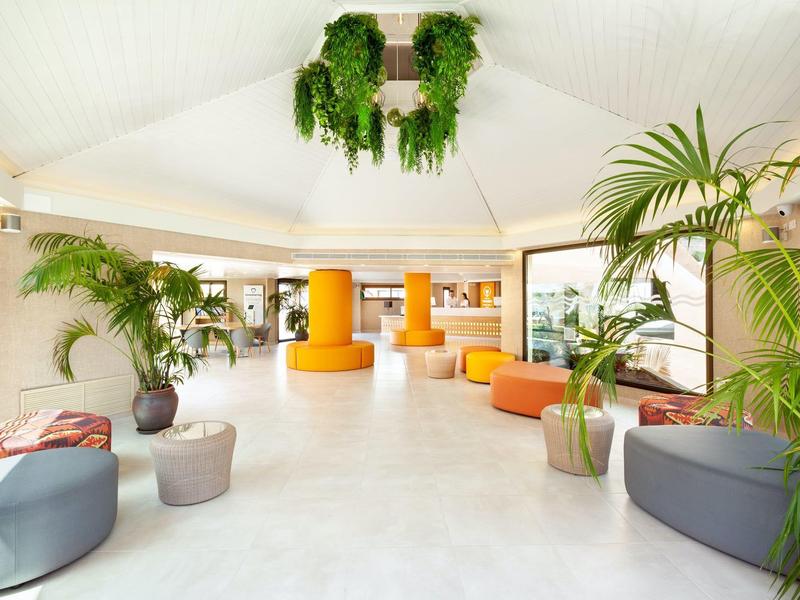 Ingresso dell'hotel luminoso con posti a sedere moderni, piante e decorazioni appese al soffitto.