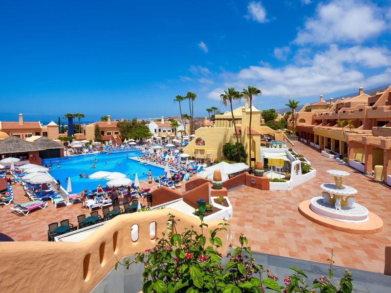 Grande piscina dell'hotel con lettini e palme sotto un cielo azzurro.