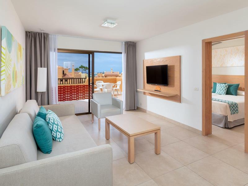 Soggiorno moderno con divano, TV a schermo piatto e vista su balcone e camera da letto.