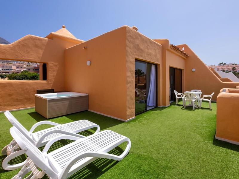 Terrazza con lettini, vasca idromassaggio e zona soggiorno circondata da muri arancioni.