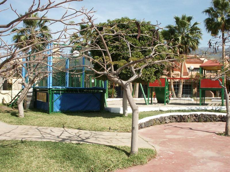 Area giochi con trampolino, altalene e alberi in un giardino dell'hotel.