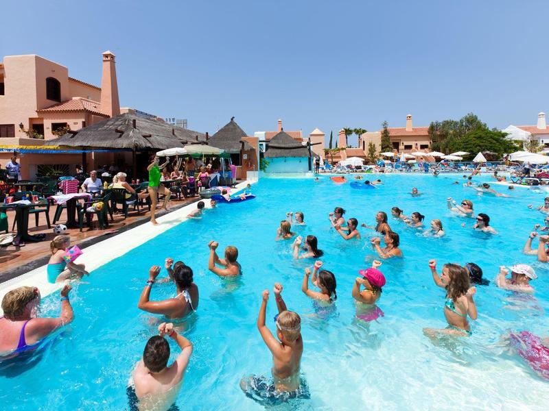 Persone che fanno ginnastica acquatica in una piscina d'hotel azzurra in una giornata limpida.