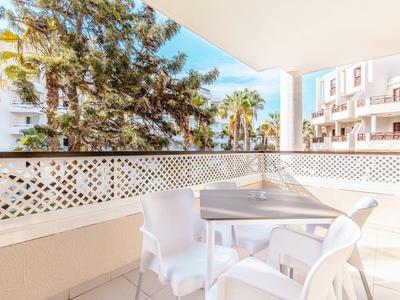 Helle Terrasse mit weißen Stühlen und Tisch, umgeben von weißem Gitterzaun und grünen Bäumen.