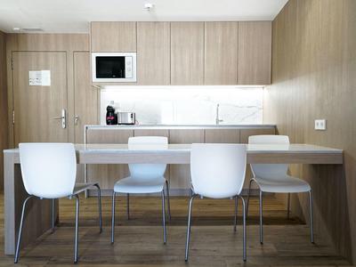 Moderner Küchenraum mit Holzmöbeln, weißen Stühlen, Kaffeemaschine und Mikrowelle an der Wand.