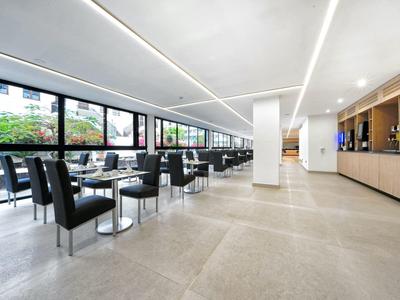 Großer heller Speisesaal mit schwarzen Stühlen, Tischen und großen Fensterfronten entlang der linken Wand.