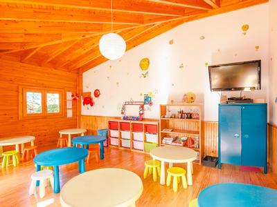 Buntes Kindergartenzimmer mit kleinen Tischen, Hockern und Holzdecke, Wand mit Dekorationen.