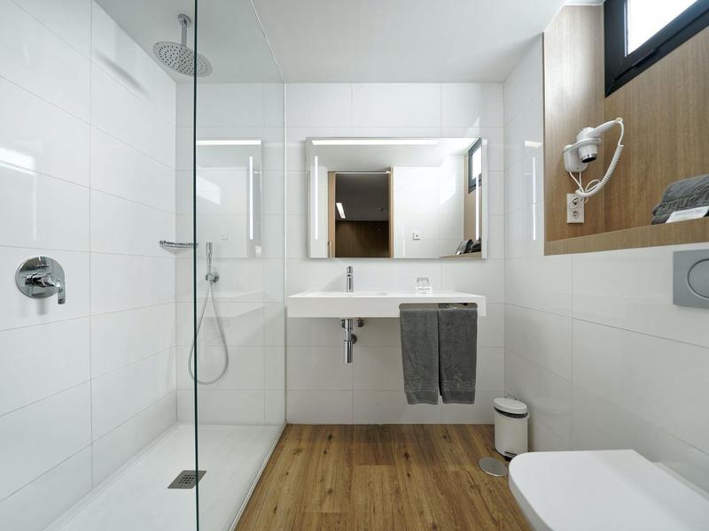 Modernes Badezimmer mit weiß gekachelten Wänden, Holzboden, Dusche, Waschbecken und Toilette.