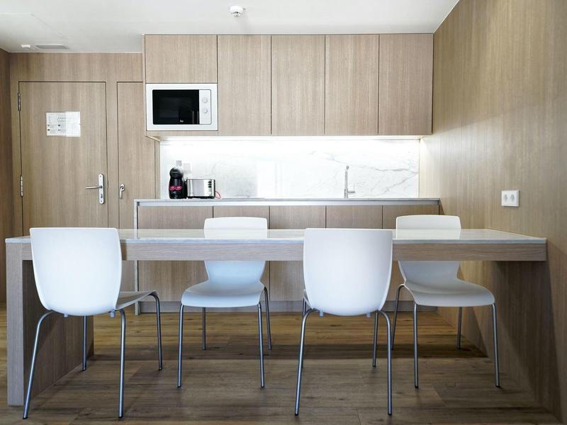 Moderner Küchenraum mit Holzmöbeln, weißen Stühlen, Kaffeemaschine und Mikrowelle an der Wand.