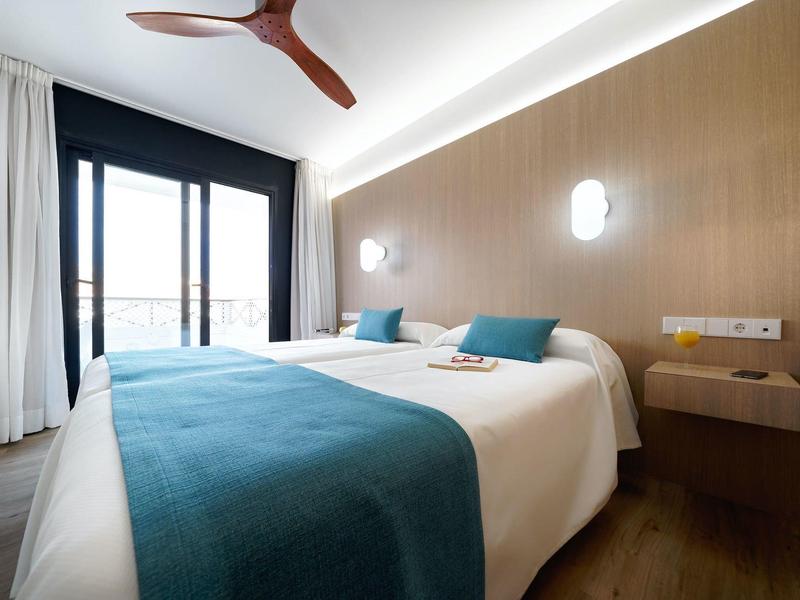 Modernes Schlafzimmer mit Doppelbett, blau-weißer Bettwäsche, Holzwand und Deckenventilator.