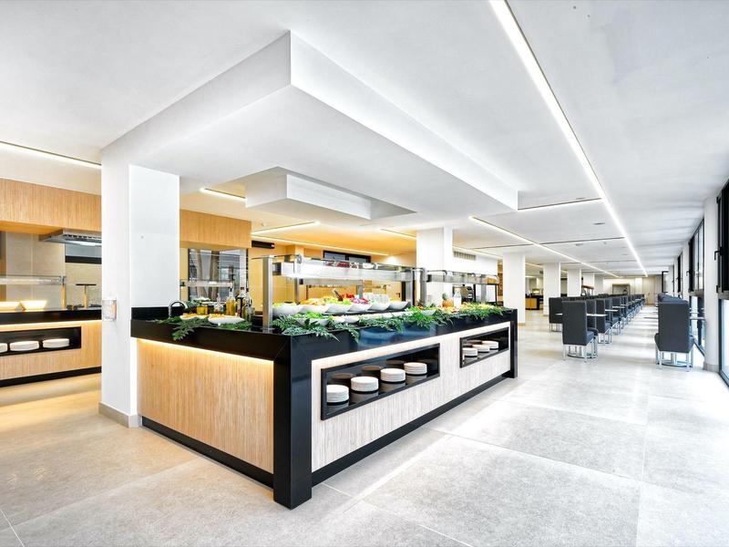 Heller moderner Supermarkt mit breiten Gängen und großen Fenstern, gut beleuchteter Obst- und Gemüsebereich.