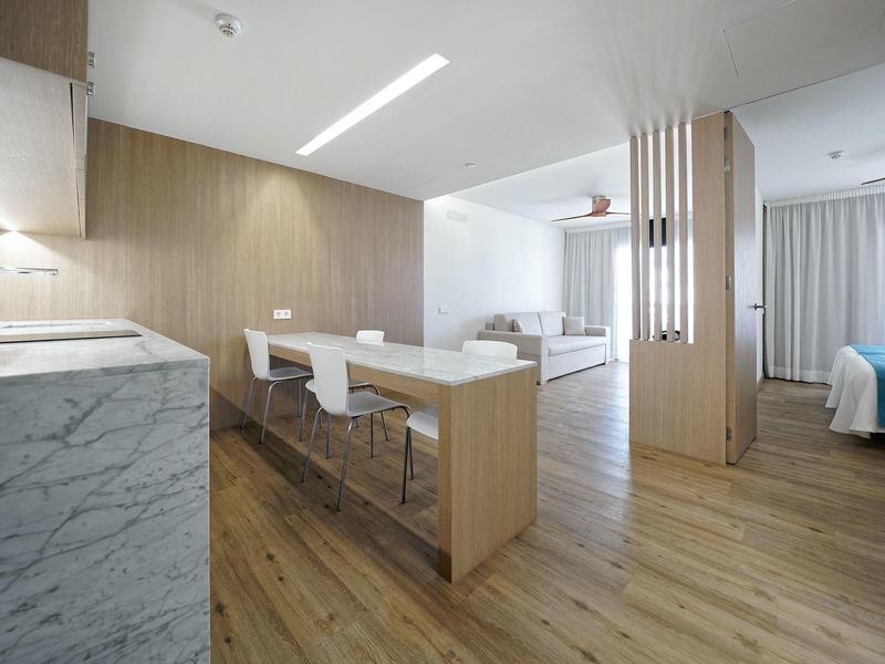 Moderne offene Küche mit Holzdekor, weißen Barhockern und Holzboden in hellem, minimalistischem Stil.