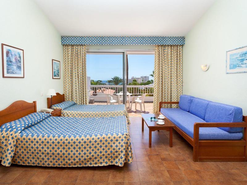 Camera d'hotel luminosa con letto matrimoniale, divano blu e balcone con vista.