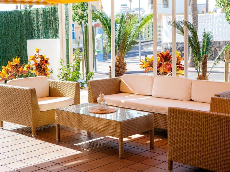 Accogliente terrazza con mobili beige imbottiti e tavolo in vetro sotto una tenda.