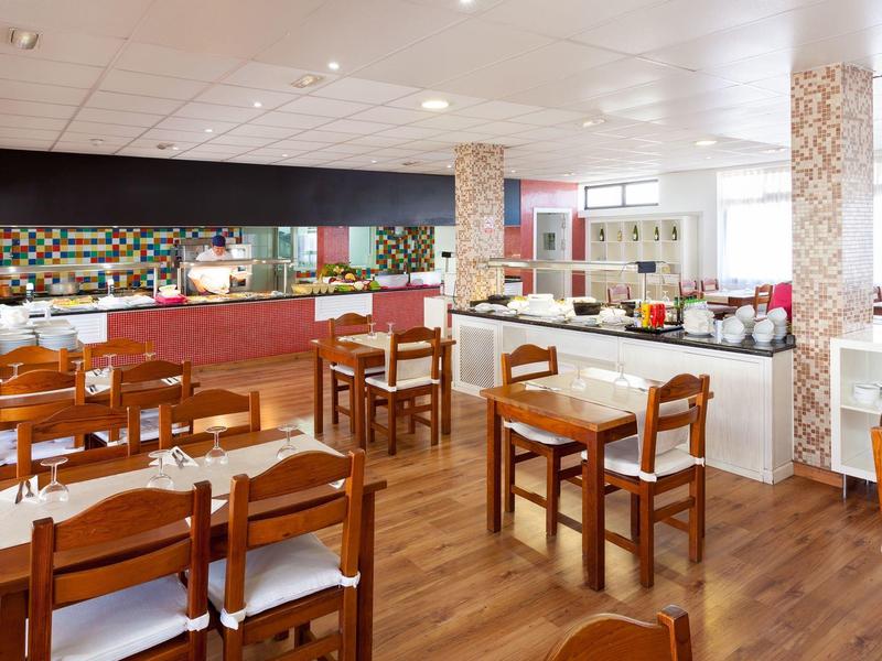 Sala per la colazione luminosa con sedie e tavoli in legno e area buffet con cibo.