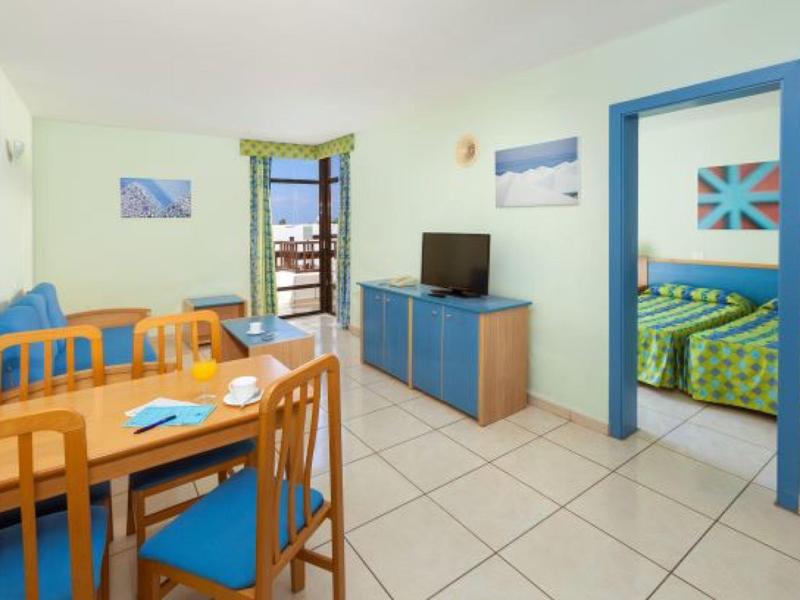 Soggiorno luminoso con tavolo da pranzo, accenti blu e camera da letto adiacente in hotel.