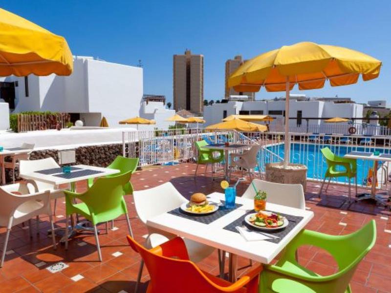 Terrazza sul tetto con sedie colorate, tavoli e ombrelloni gialli sotto un cielo azzurro.
