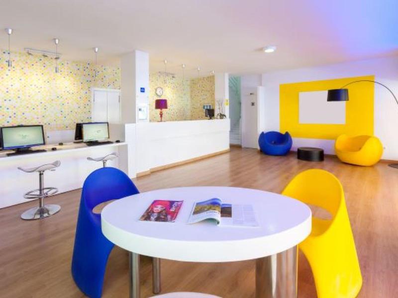 Luminoso lobby dell'hotel con sedute colorate, reception e computer sul muro.