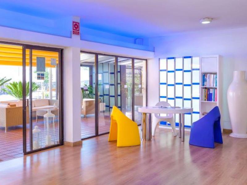 Locale luminoso con pavimento in legno, pouf colorati e vista su terrazza con mobili lounge.