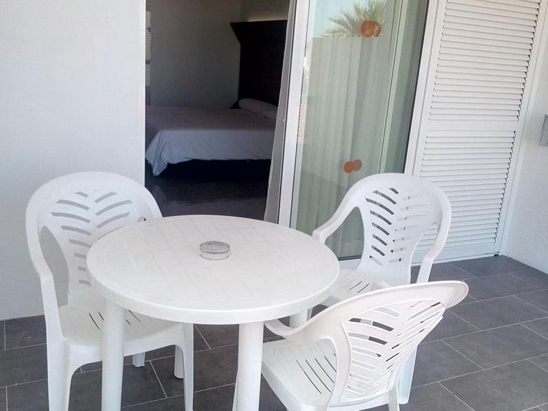 Piccolo patio con tavolo rotondo in plastica bianca e tre sedie davanti a una porta scorrevole aperta.