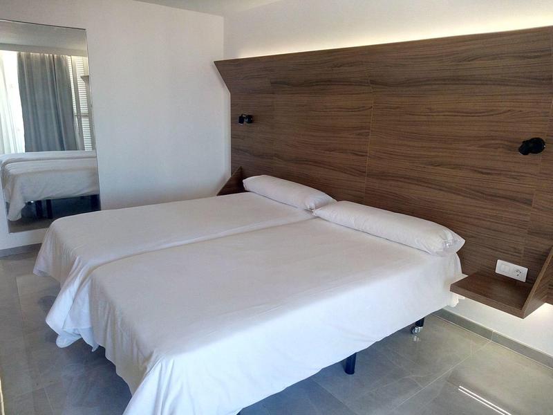 Due letti singoli con lenzuola bianche contro una parete in legno in una camera d'hotel moderna.