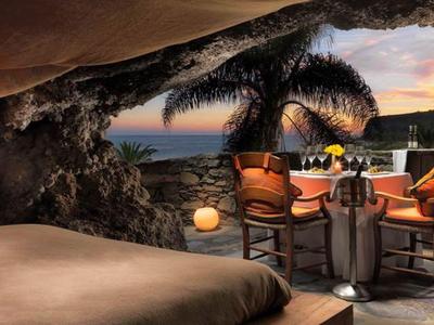 Offener Restaurantbereich mit Holzmöbeln, Pflanzen und Blick auf den Sonnenuntergang am Meer.