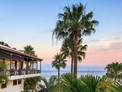Blick auf ein Hotel mit Palmen und Meer bei Sonnenuntergang.