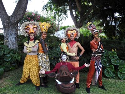 Vier Personen in bunten Kostümen und Masken posieren im Freien vor grüner Vegetation.