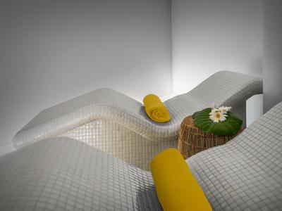 Wygodne leżaki z białymi pokrowcami, żółtymi ręcznikami i małym drewnianym stolikiem z rośliną.