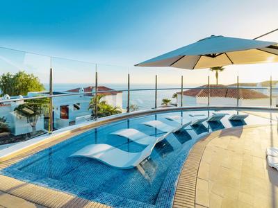 Poolbereich mit Liegen und Sonnenschirm mit Blick auf das Meer bei Sonnenuntergang.