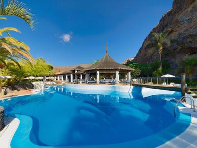 Duży niebieski basen z palmami i górami w tle w ośrodku hotelowym.