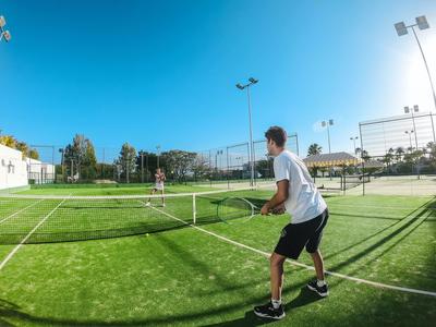 Junger Mann spielt Tennis auf einem sonnigen, grünen Tennisplatz.