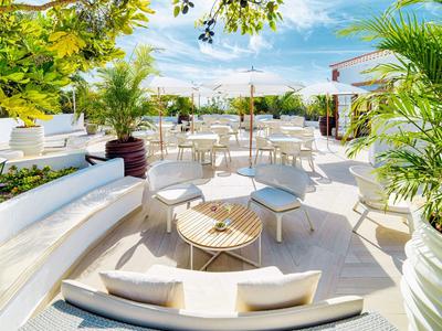 Jasny, nowoczesny taras na dachu z białymi meblami i zielonymi roślinami pod błękitnym niebem.