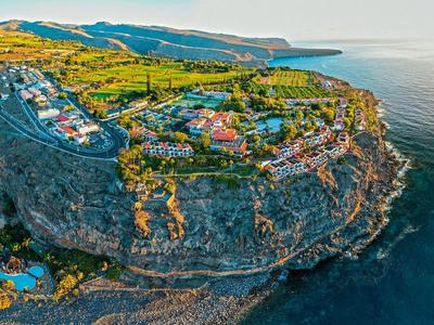 Ośrodek hotelowy na klifie z widokiem na morze i okoliczny krajobraz o zachodzie słońca.