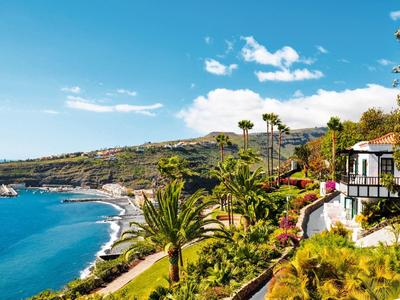 Widok na wybrzeże z palmami, domami i morzem pod jasnym niebem.