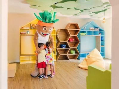 Dzieci przytulają osobę w kostiumie warzywa w kolorowej, nowoczesnej sali zabaw.