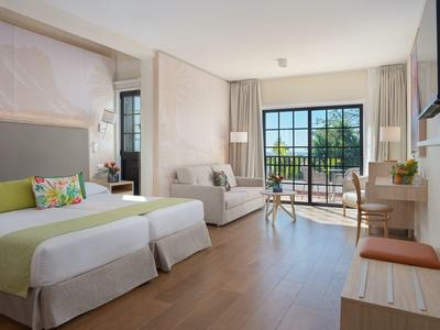 Nowoczesny pokój hotelowy z łóżkiem podwójnym, częścią wypoczynkową i balkonem z widokiem.