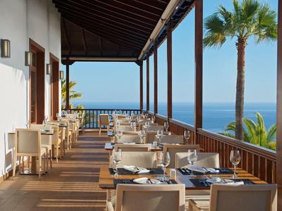 Taras restauracji z widokiem na morze, nakryte stoły i palmy.