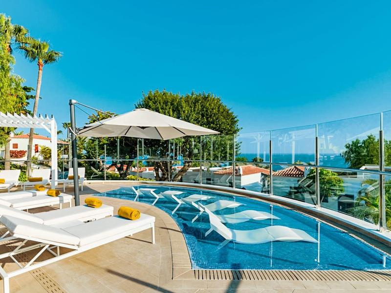 Obszar basenu z leżakami i parasolami pod niebieskim niebem w miejscu wakacyjnym.